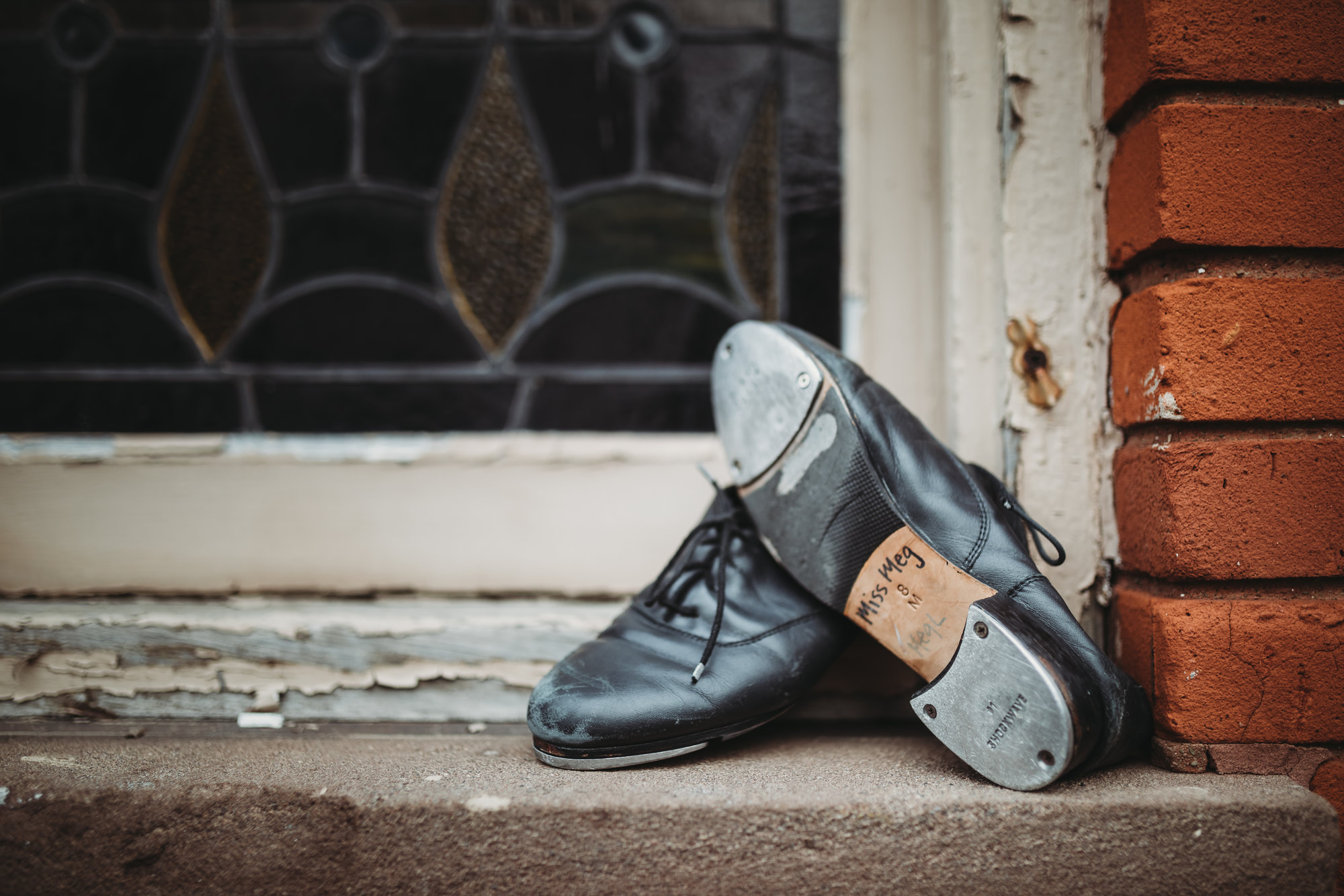 Miss Meg's black tap shoes resting on a windowsill, labeled 'Miss Meg 8 M'