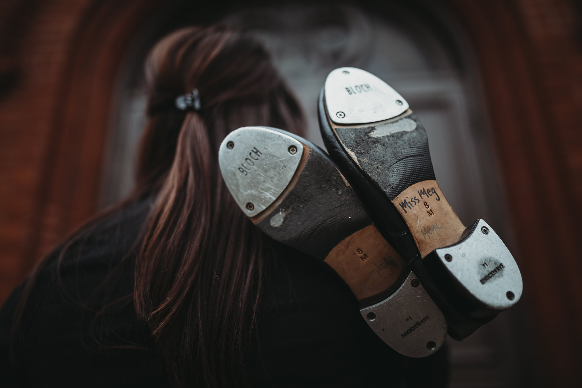 Miss Meg holding her well-worn tap shoes over her shoulder